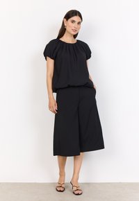 Svart kortärmad topp med samlad hals, parat med vida svarta byxor. Slät tyg med avslappnad passform. Svarta remsandaler.