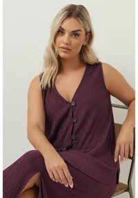 Lila, ärmlös topp med V-ringning och textil med en strukturerad herringbone-mönster; fem knappar framtill.