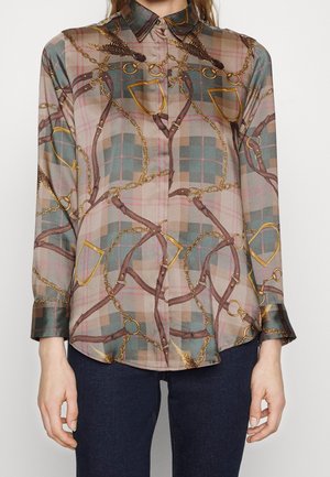 Langärmeliges Hemd mit Knopfleiste, grün-beige-braut kariert mit goldenen Ketten und braunen Lederbändern, getragen zu dunklen Jeans.