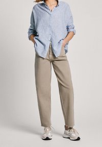 Blue and white striped button-up shirt with a relaxed fit, paired with light beige pants and white sneakers with grey accents.