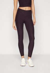 Høyt liv purple tights laget av et teksturert, elastisk materiale, kombinert med en matchende cropped topp og hvite sportssko.