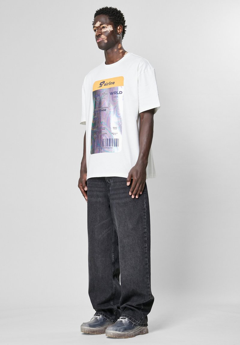 Hvit grafisk t-skjorte med design av flybillett, svarte jeans og gjennomsiktige joggesko. T-skjorten har et holografisk trykk.