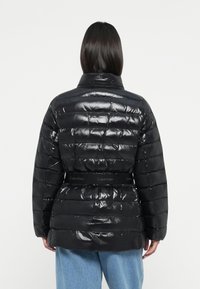 Zwarte pufferjack met een glanzende textuur, horizontaal gestikte ontwerpen en een gemerkte riem op de taille. Hoge kraag en lange mouwen.