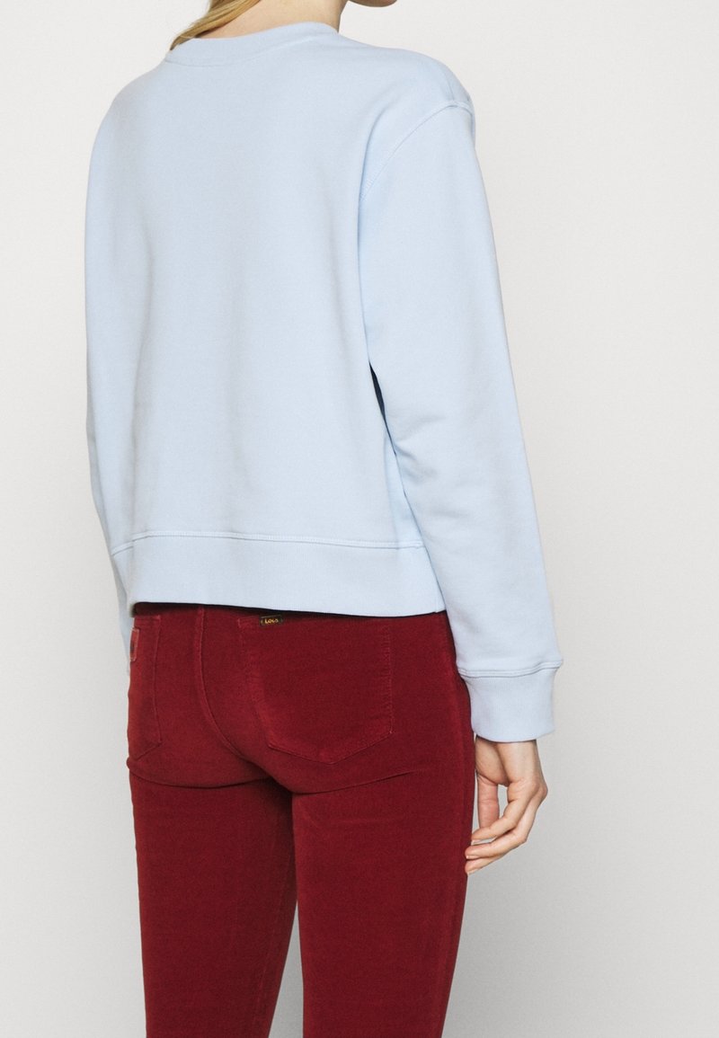 Sweatshirt court bleu clair à manches longues, avec poignets côtelés et encolure ronde. Associé à un jean skinny rouge foncé.