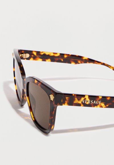 Lunettes de soleil Versace à motif écaille avec des verres carrés foncés et le logo Medusa doré sur le coin de la monture et la branche.