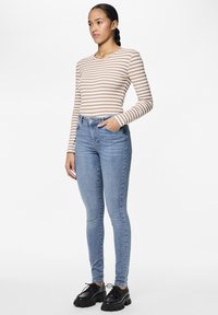 Gestreepte langemouwen top in beige en wit, gecombineerd met lichtblauwe skinny jeans. Schoeisel heeft robuuste zwarte zolen en veters.