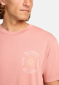 Light pink t-shirt made of cotton featuring a round neckline and short sleeves; front graphic includes the text "Billabong" and a sun design.