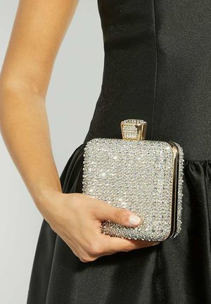 Sparkling silver clutch made of rhinestones, rectangular shape with a gold clasp, held in a hand against a black dress.