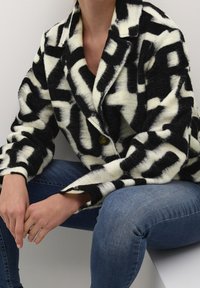 Svart och vit mönstrad kavaj med slagkrage, med knappstängning och avslappnad passform; bärs över jeans.