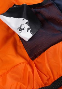 Oranges Nylonstoff mit einem Netzbereich. Schwarz-weißes Grafikdesign mit einer Spinne. Strukturiert Oberfläche mit genähten Nähten.