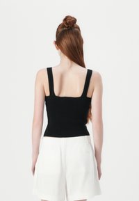 Top negru din tricot, cu bretele late, formă ajustată, textură cu nervuri și decolteu pătrat la spate. Asortat cu pantaloni scurți albi.