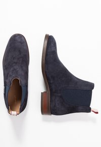 Marineblauwe suède Chelsea boots met elastische zijkanten en een pull-tab. Bruine leren zool en een gladde textuur. Minimalistisch ontwerp.