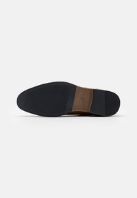 Suola di scarpa in pelle marrone con una superficie liscia e leggermente strutturata, suola in gomma con battistrada e un delicato dettaglio di cucitura.