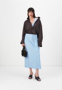 Chemise oversize à rayures noires et blanches, robe en satin bleu clair, sandales à plateforme noires et petit sac à main noir avec accent blanc.