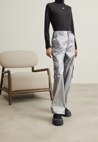 Metallic silver cargobyxor med sidofickor, hög midja och avslappnad passform, tillsammans med en åtsittande svart långärmad topp och skoinlägg.