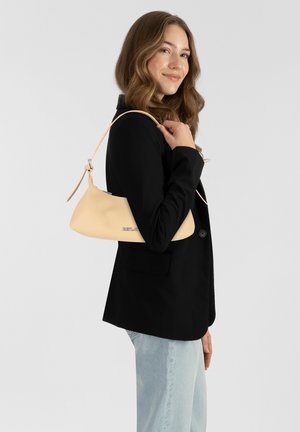 Beige leren handtas met een gebogen silhouette en een verstelbare band, met een subtiel logo. Draag onder de arm met een zwarte blazer.