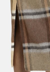 Vilnas svārki ar plaid rakstu bēšā, brūnā un pelēkā toņos, ar šķēlumu, demonstrējot mīkstu tekstūru un slāņveida dizainu.