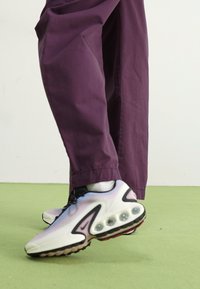 Nike sneakers feature a multicolored textured upper with prominent air cushioning, paired with loose-fitting purple trousers.