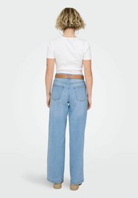 Světle modré džíny s širokými nohavicemi a vysokým pasem, se dvěma zadními kapsami a hnědým páskem, v kombinaci s přiléhavým bílým krátkým topem s krátkým rukávem.