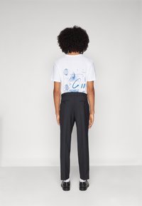 Weißes T-Shirt mit blauem Grafikelement auf der Rückseite, kombiniert mit schwarzen Hosen und schwarzen Schuhen; glatte Textur, lässige Passform.