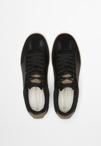 Czarne sneakersy wykonane z połączenia gładkiej skóry i zamszu. Wyposażone w czarne sznurowadła, brązowe akcenty oraz wyściełaną wkładkę z logo.