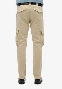 Beige cargobroeken met twee zijzakken, achterzakken en een taps toelopend pootontwerp. Gemaakt van geweven stof, met een zachte textuur.