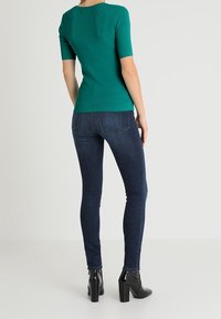 Teal ribbed knit top with short sleeves paired with form-fitting dark blue jeans and black high-heeled ankle boots.