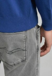 Maglione blu con polsini a coste, abbinato a jeans grigi con motivo cucito sulla tasca posteriore e chiusura con bottone metallico.