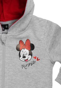Felpa grigia con zip e fodera interna rossa, decorata con un'immagine del volto di un personaggio e la scritta "Minnie" in nero, con cuori rossi come accento.