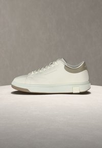 Λευκό αθλητικό παπούτσι χαμηλού προφίλ με μπεζ λεπτομέρειες, δέσιμο με κορδόνια και παχύ πέλμα με ανάγλυφο λογότυπο στο πλάι.