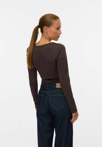 Langarm bruine top met een aangesloten ontwerp, gecombineerd met donkere spijkerbroek met wijde pijpen en een leren patch op de tailleband en achterzakken.
