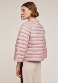 Jachetă roz, pufoasă, cu un design matlasat orizontal, guler înalt și mâneci scurte. Textură netedă și finisaj lucios.