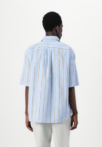 Camisa de manga corta en tejido azul claro con rayas verticales en naranja y blanco. Presenta un cuello clásico y un corte holgado.