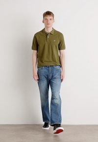 Olivengrøn polo skjorte med korte ærmer, lyseblå denim jeans og sorte sneakers med hvide såler. Enkel design, ingen mønstre eller detaljer.