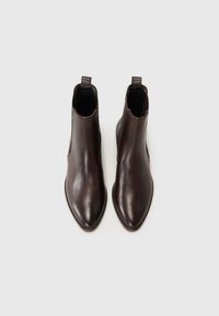 Bottines en cuir marron avec un bout pointu, des panneaux latéraux élastiques et des languettes de traction, présentant une texture lisse et un design minimaliste.