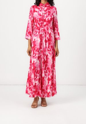 Woman wearing long-sleeve, ankle-length buttoned dress with pink, red, and white abstract pattern and open-toe beige sandals.