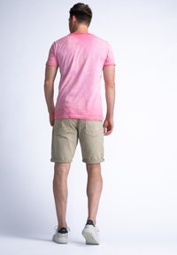 Camiseta de manga corta rosa con una textura suave, combinada con pantalones cortos beige claros, arremangados, y zapatillas blancas con acentos oscuros.
