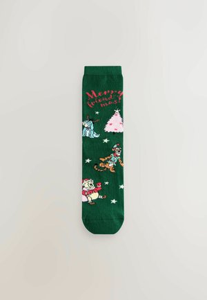 Green socks featuring holiday-themed designs: a pink Christmas tree, snowflakes, and characters, including a Santa bear and others.