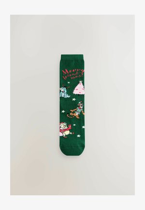 Grüne Socken mit festlichen Designs: ein pinker Weihnachtsbaum, Schneeflocken und Figuren, darunter ein Weihnachtsmann-Bär und andere.