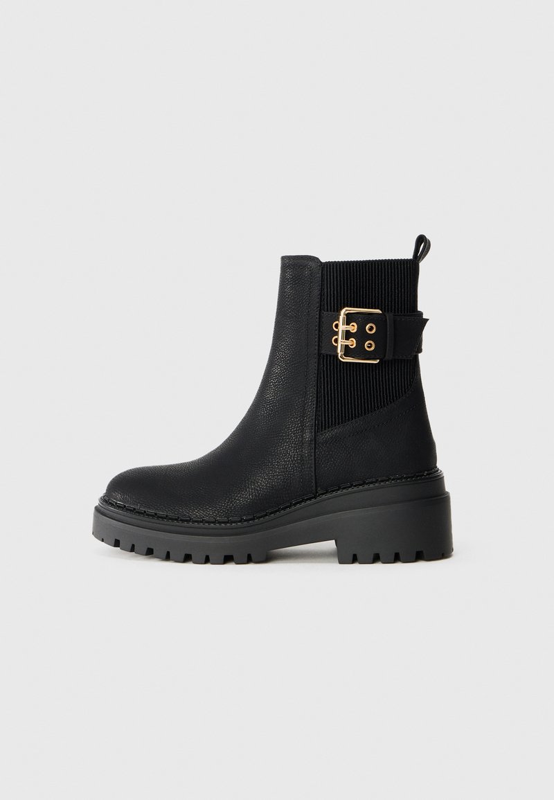 Bottines noires avec tige en cuir texturé, panneau élastique à côtes et accent en boucle dorée. Semelle en caoutchouc chunky avec motif pour l'adhérence.