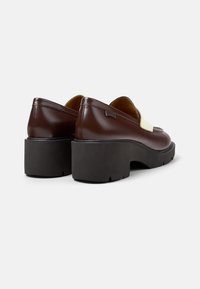 Zapatos de cuero marrón con una suela de plataforma negra elevada, que presenta un acento beige en la parte delantera y un logo sutil en el costado.