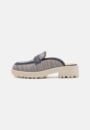 Buty typu mule wsuwane z teksturowaną szarą cholewką z tkaniny, czarnym obszyciem, dekoracyjnym metalowym detalem i masywną beżową gumową podeszwą.