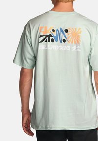 Mentolová bavlněná tričko s barevnými abstraktními grafikami na zadní straně, s nápisem "BILLABONG", krátkými rukávy a volným střihem.