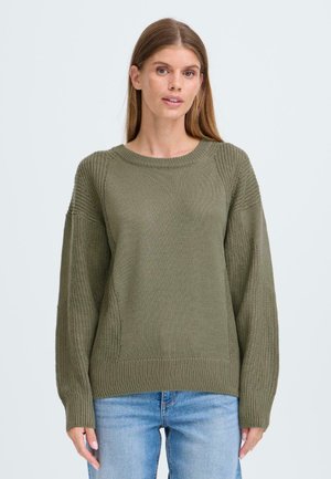 Pull olive vert avec un design en tricot texturé, doté de manches raglan et de poignets et ourlet côtelés. Associé à un jean en denim bleu.