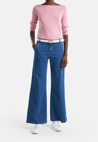 Pink long-sleeve top paired with wide-leg blue denim jeans and a white belt. The outfit is completed with white sneakers.