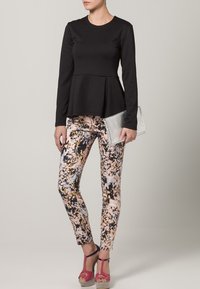 Haut noir à manches longues avec un design en peplum, associé à des leggings ajustés à motifs floraux multicolores et des sandales à plateforme roses, tenant une pochette argentée.