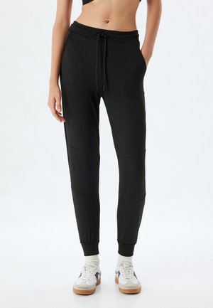 Schwarze Jogginghosen mit Kordelzugbund, Seitentaschen, elastischen Bündchen und glatter Textur; mit Paneel-Details an den Beinen.