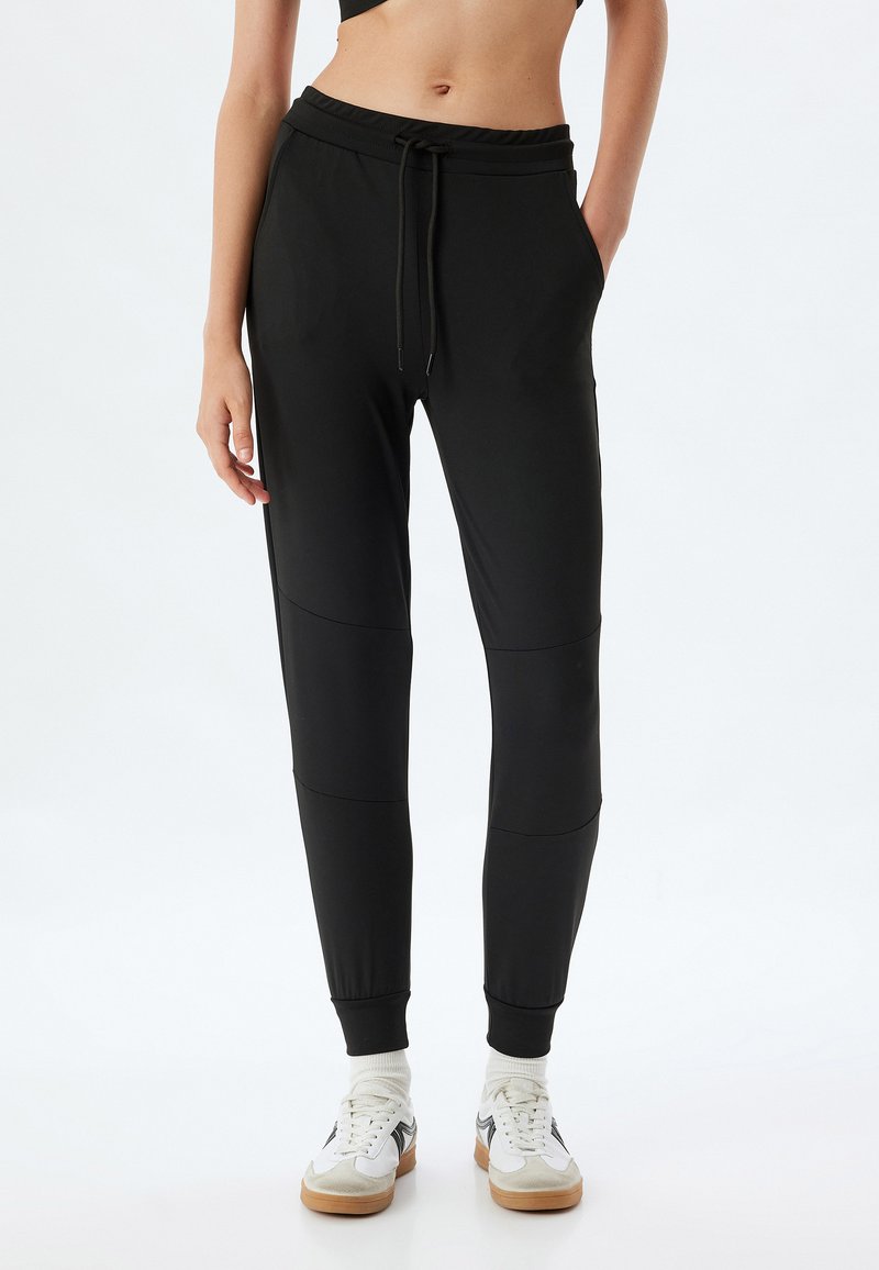 Schwarze Jogginghosen mit Kordelzugbund, Seitentaschen, elastischen Bündchen und glatter Textur; mit Paneel-Details an den Beinen.