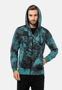 Tealfarbener Zip-Hoodie mit schwarzem Grafikdruck, der ein Vintage-Motorrad-Design und Text zeigt. Aus weichem Material, mit gerippten Bündchen und Saum.