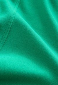 Gros plan d'un tissu bleu sarcelle vif montrant la texture tricotée et les coutures avec des plis doux et des ombres.